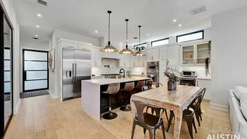 A modern kitchen with a central island, stainless steel appliances, pendant lighting, and a dining area with wooden chairs.