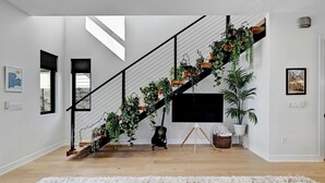 A modern staircase with plants, a flat-screen TV, and a large white rug.