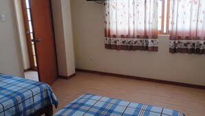 A room with two beds, a TV mounted on the wall, and a window with floral curtains.