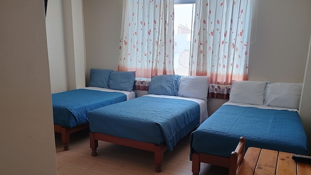 A room with three wooden beds, each with blue bedding. The room has wooden flooring and a wooden table.