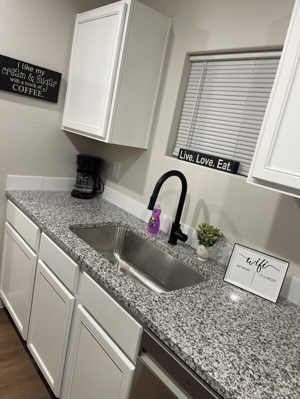 A kitchen with white cabinets, a granite countertop, a coffee maker, a sink, and a sign that says "Live. Love. Eat." - Pristine new 3-bedroom house in Odessa with AC, WiFi (Odessa)
