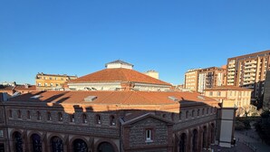 Un edificio histórico con tejado de tejas y ventanas arqueadas, situado en una zona urbana con edificios modernos cercanos.