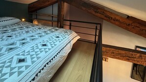 Un dormitorio tipo loft con techo inclinado, una cama con ropa de cama estampada y un tragaluz.