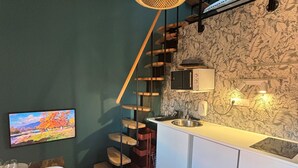 Una cocina funcional con una escalera de madera, un comedor con mesa y sillas, y un televisor fijado a la pared.