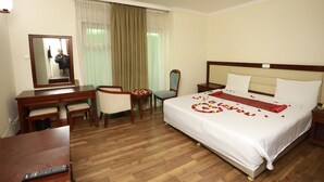 Ein Hotelzimmer mit einem Bett, einem Schreibtisch, einem Stuhl, einem Spiegel und einem Fenster mit Vorhängen.