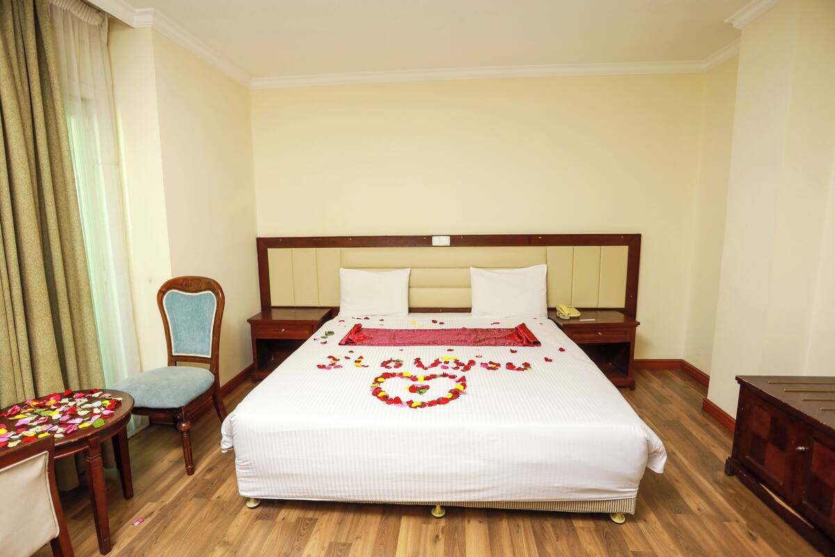 Una habitación de hotel con una cama grande, una mesita de noche de madera, una silla y un escritorio.