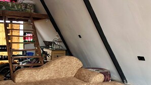 A loft-style room with a sloped ceiling, a wooden ladder, a sofa, and a small white table with a flag design.