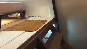 A room with a bed, a small table, and a brown rug. There is a visible power outlet and a light switch on the wall.