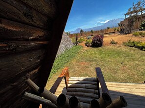 Eine Holzterrasse mit Baumstämmen, einem Rasen und Blick auf die Berge.