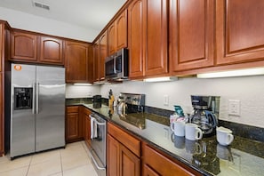 Una cocina con gabinetes de madera, electrodomésticos de acero inoxidable, encimera de granito y cafetera.