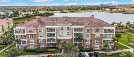 A multi-story residential building with a central courtyard, parking lot, and a lake in the background.