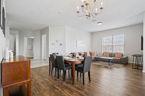 A spacious living area with a dining table set for four, a sofa, and a chandelier.