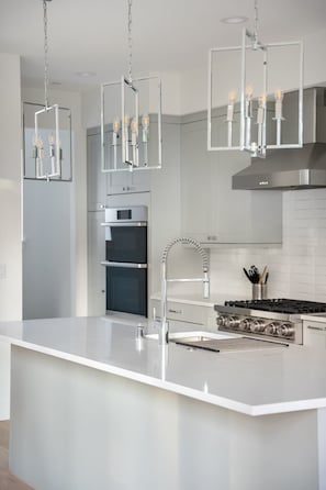 A modern kitchen with a large island, stainless steel appliances, and pendant lighting.
