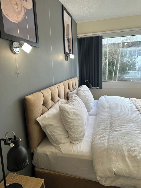 A neatly made bed with white bedding, a tufted headboard, and a bedside lamp.