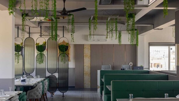A restaurant with green booths, hanging plants, and a ceiling fan.