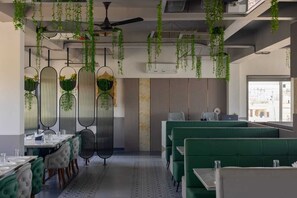 A restaurant with green booths, hanging plants, and a ceiling fan. - Shivam Hotel-Madhavpur (Porbandar)