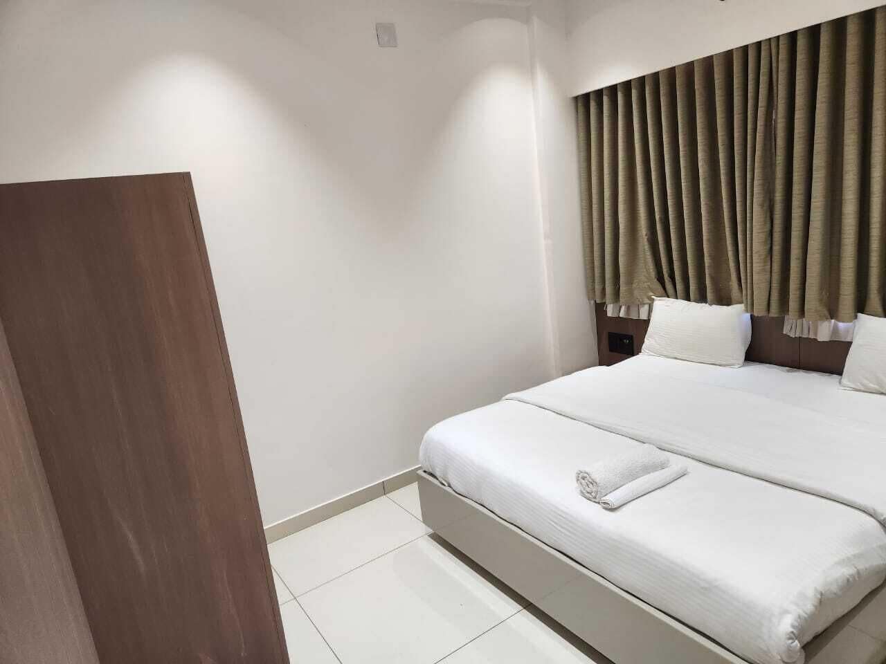 Une chambre d’hôtel avec un grand lit, du linge de lit blanc, une porte en bois et un rideau.