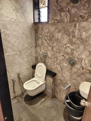 A compact bathroom with a toilet, bidet, and black trash bin. - Shivam Hotel-Madhavpur (Porbandar)