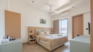 A modern hotel room with a large bed, a bedside table, a desk, and a window with curtains.