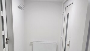 A narrow hallway with a radiator, a black doormat, and white walls. - Vu's Home - Apartment Garden - 30m2 (Hlavní město Praha)
