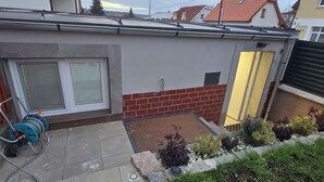 A residential building with a tiled patio, a garden with various plants, a blue garden hose, and a red fence. - Vu's Home - Apartment Garden - 30m2 (Hlavní město Praha)