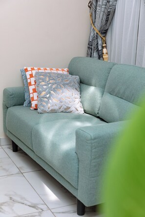 Relax in this inviting living room with a sofa, decorative pillows, and a window with a leaf-patterned curtain.