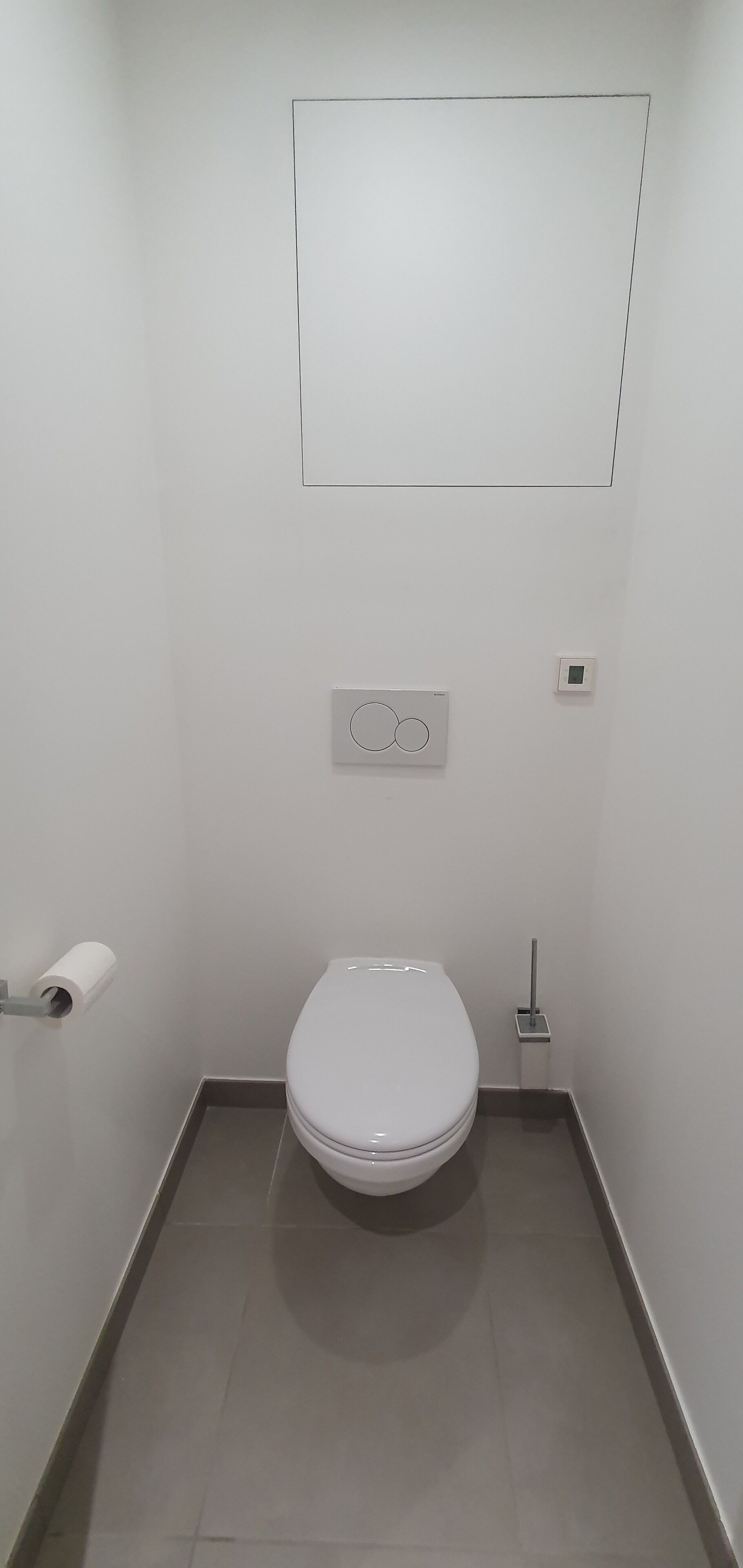Een kleine, schone badkamer met een toilet, toiletrolhouder, spoelknop en een toiletmodel dat op de vloer staat.