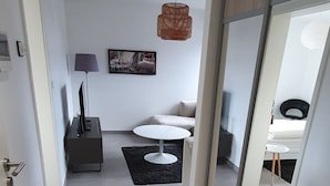 Une chambre d’hôtel moderne dotée d’une porte coulissante, d’un téléviseur à écran plat, d’une lampe, d’un canapé et d’une petite table.