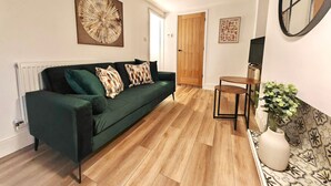 A living room with a dark green sofa, wooden flooring, a small wooden table, and a large abstract painting on the wall. - Prime Exeter Stay for Corporate & Family Guests (Exeter)