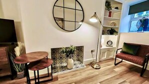 A living room with a round mirror, a round table, a sofa, a floor lamp, and a fireplace with a patterned backsplash. - Prime Exeter Stay for Corporate & Family Guests (Exeter)
