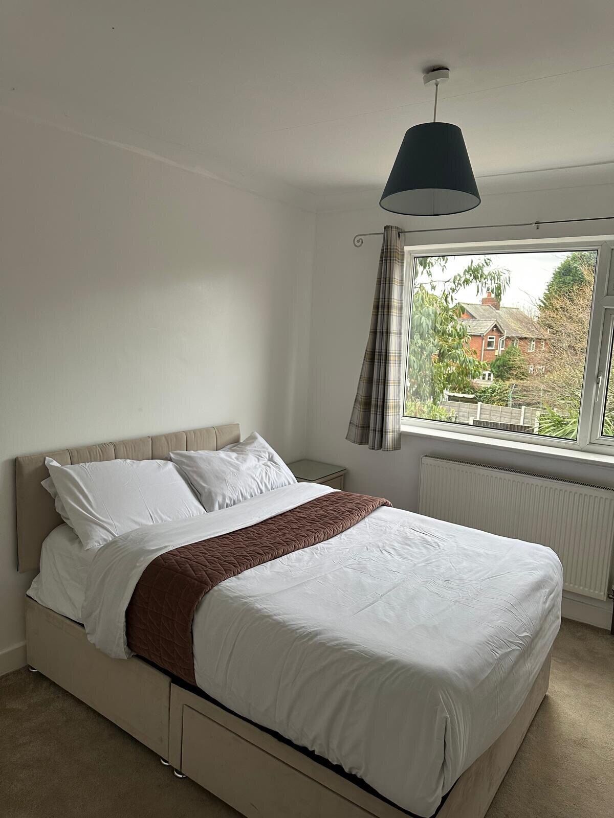 A bedroom with a bed, a window with curtains, a radiator, and a hanging light fixture.