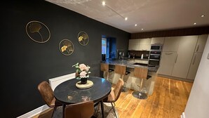 Una cocina moderna con una isla central, una zona de comedor con una mesa redonda y sillas, y una pared oscura decorada con elementos artísticos.