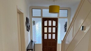 Un pasillo con suelo de madera, una puerta con paneles de vidrio esmerilado y una lámpara colgante amarilla.
