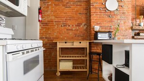 Une cuisine avec un mur en briques, un fourneau blanc, un four à micro-ondes et une étagère en bois.