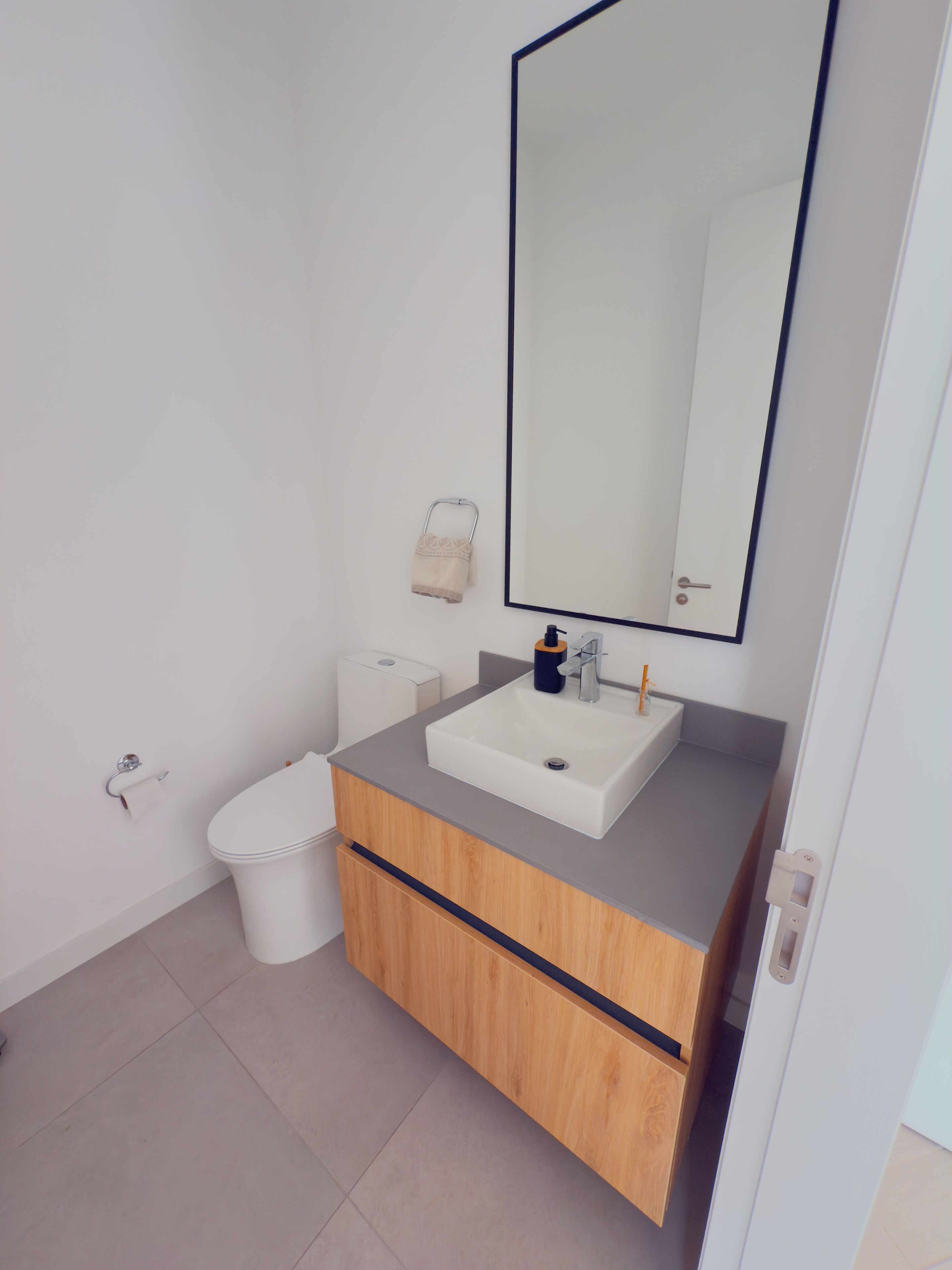 Une salle de bain moderne avec un lavabo blanc, un meuble-lavabo en bois et un grand miroir.