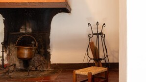 A rustic kitchen with a brick oven, a hanging pot, and a wooden chair. - Anna's home  (Torri)