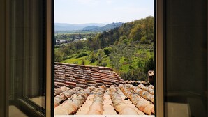 A view through an open door of a room with a tiled floor and a window overlooking a hilly landscape with a distant building. - Anna's home  (Torri)