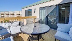 Una terraza con una mesa redonda y dos sofás, un cerco de madera y un edificio con balcones al fondo.