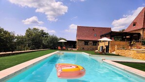 A swimming pool with a floating ring, surrounded by a stone wall and a grassy area.