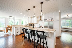 A modern kitchen with a large island, bar stools, stainless steel appliances, and pendant lighting.