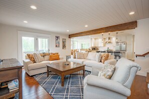 A spacious living room with a large sectional sofa, a coffee table, and a kitchen in the background.