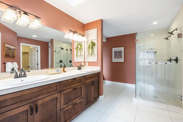 A modern bathroom with a large vanity, a glass shower enclosure, and a framed artwork on the wall.