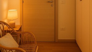 A room with a wooden door, a wicker chair, a bedside lamp, and a wall-mounted air conditioner.