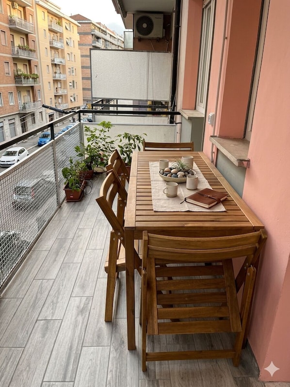 A wooden table with chairs on a balcony with a view of a cityscape.