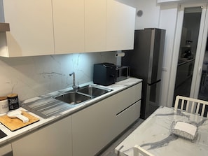 A modern kitchen with a stainless steel sink, a black coffee machine, and a refrigerator.