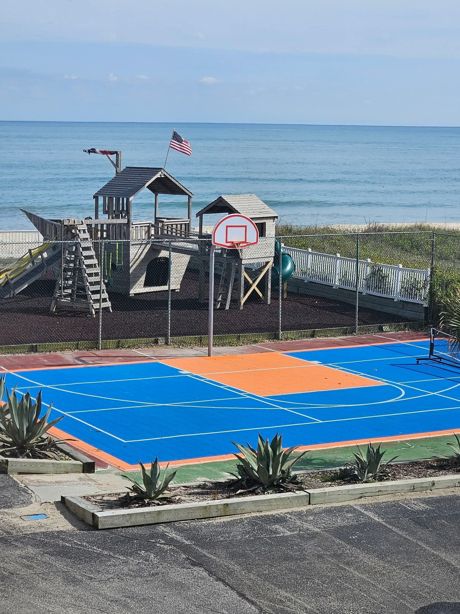 Un terrain de basket-ball doté d’une structure en bois, d’un drapeau et offrant une vue sur l’océan.
