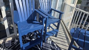 A balcony with two blue Adirondack chairs, a patterned rug, and a view of a building.