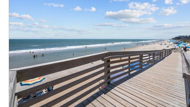 A wooden boardwalk leading to a beach with a clear sky and a few clouds.