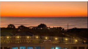 A pool area with a view of the ocean at sunset.