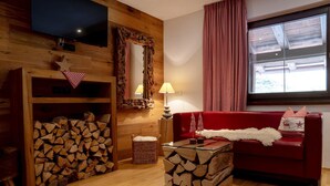 Una habitación acogedora con un sofá rojo, una mesa de centro de madera, un televisor, un espejo y una ventana con cortinas rojas.